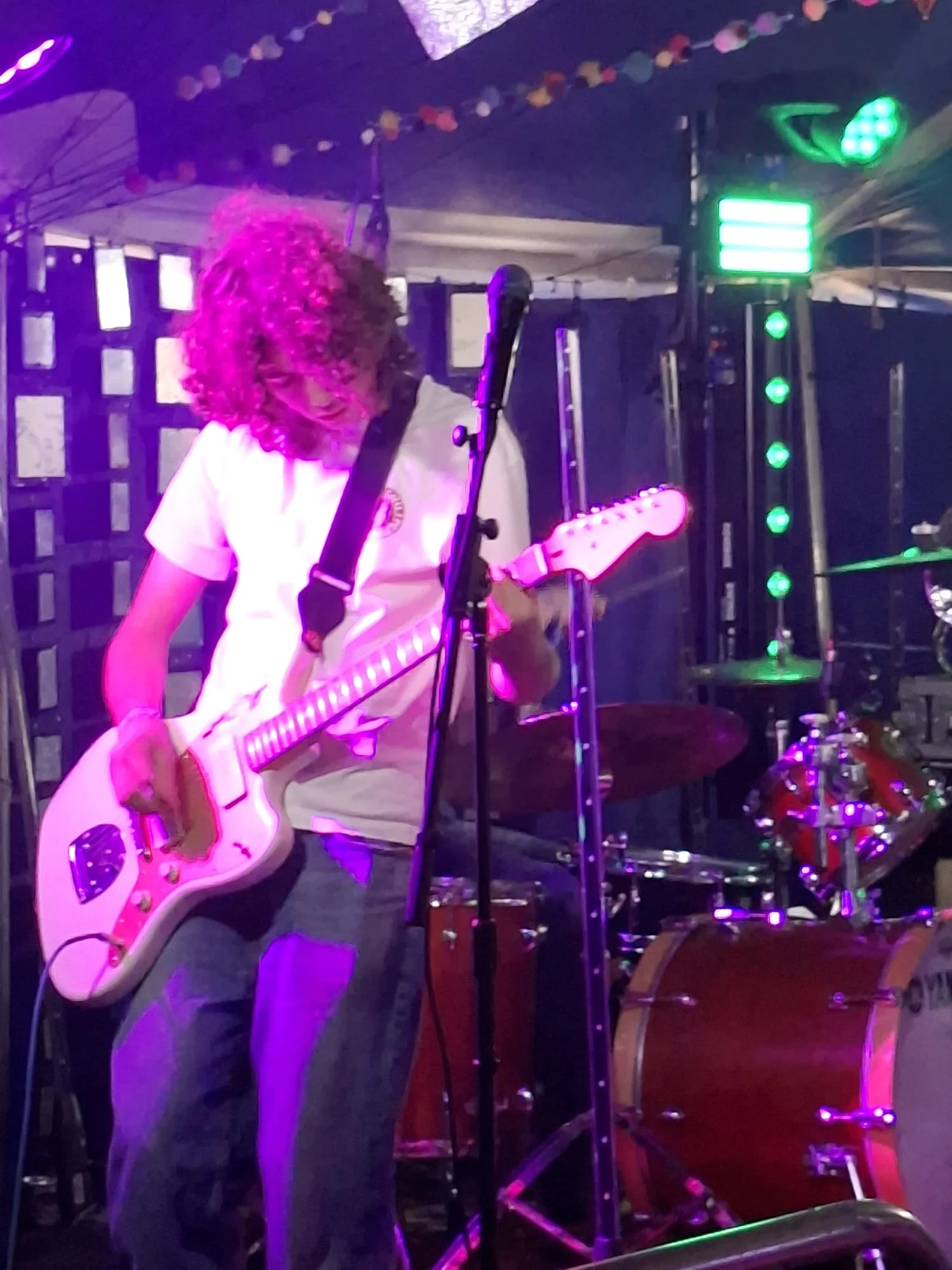 An Aphid guitarist performing with a white guitar under magenta and green lights