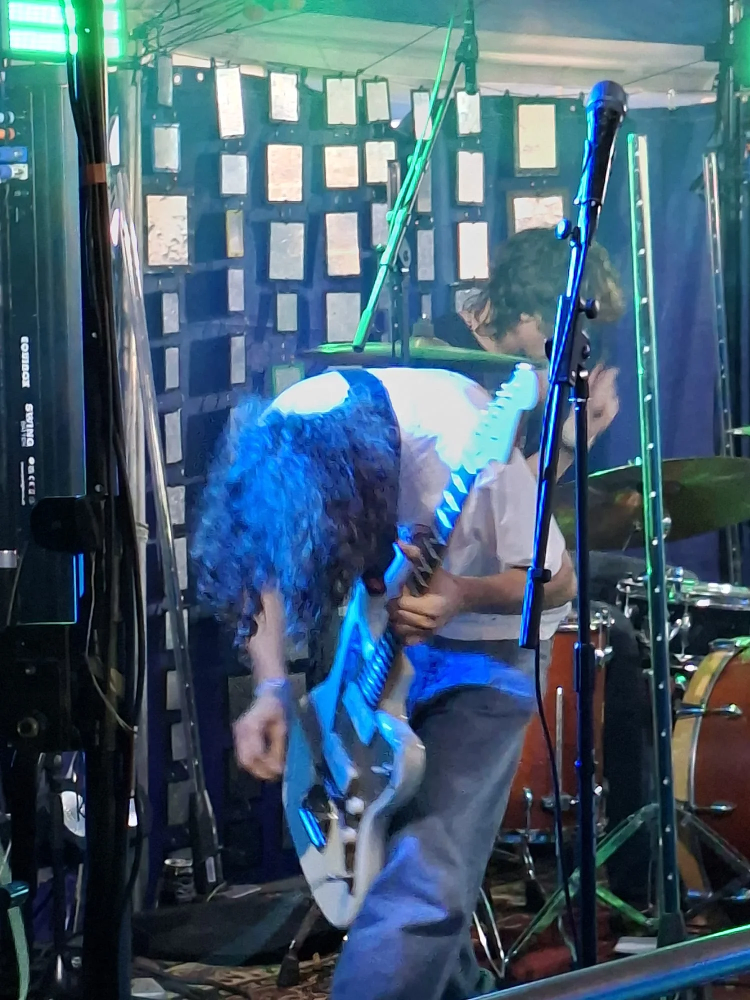 An Aphid guitarist bending into a performance under cyan lighting